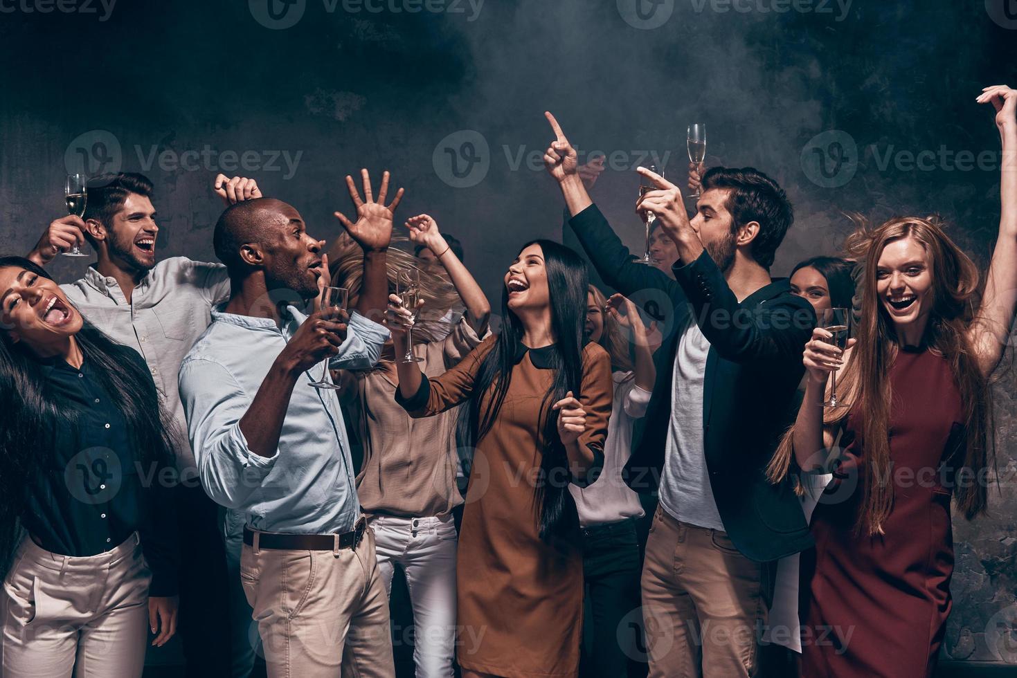 godendo sorprendente festa. gruppo di bellissimo giovane persone danza con Champagne flauti e guardare contento foto