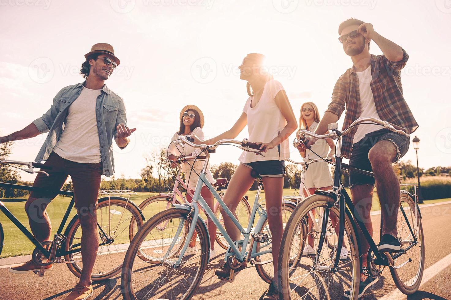 amici volontà essere gli amici. Basso angolo Visualizza di allegro giovane persone parlando mentre in piedi vicino loro biciclette su il strada foto