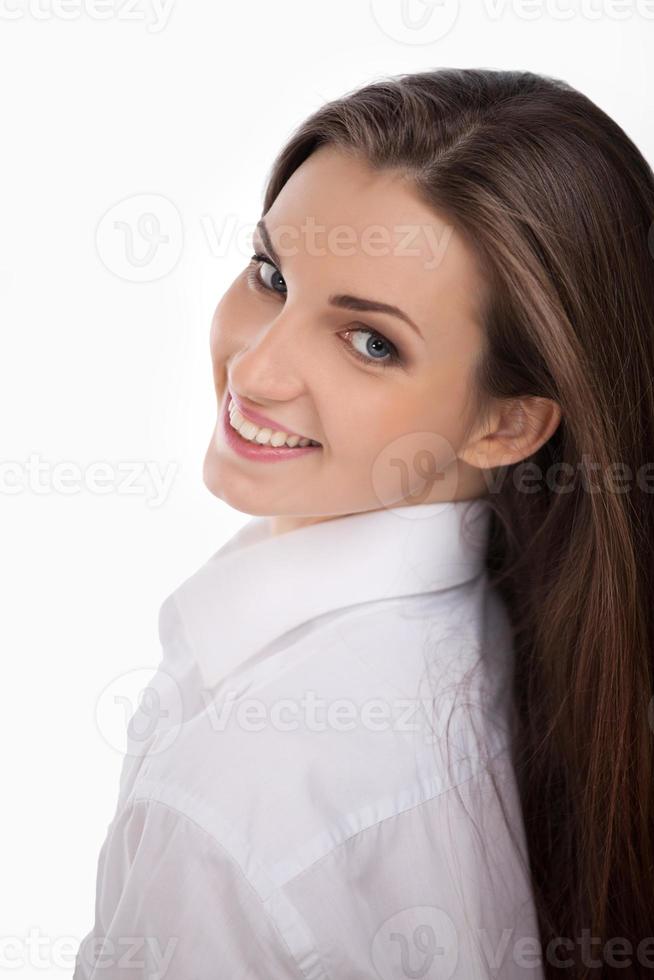 giovane e Bellissima. bellissimo giovane donna nel bianca camicia guardare al di sopra di spalla e sorridente mentre isolato su bianca foto