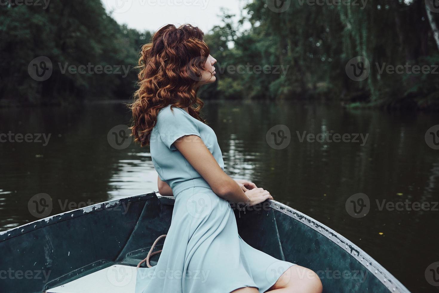 abbastanza contemplazione. bellissimo giovane donna nel elegante vestito guardare lontano mentre seduta nel il barca foto