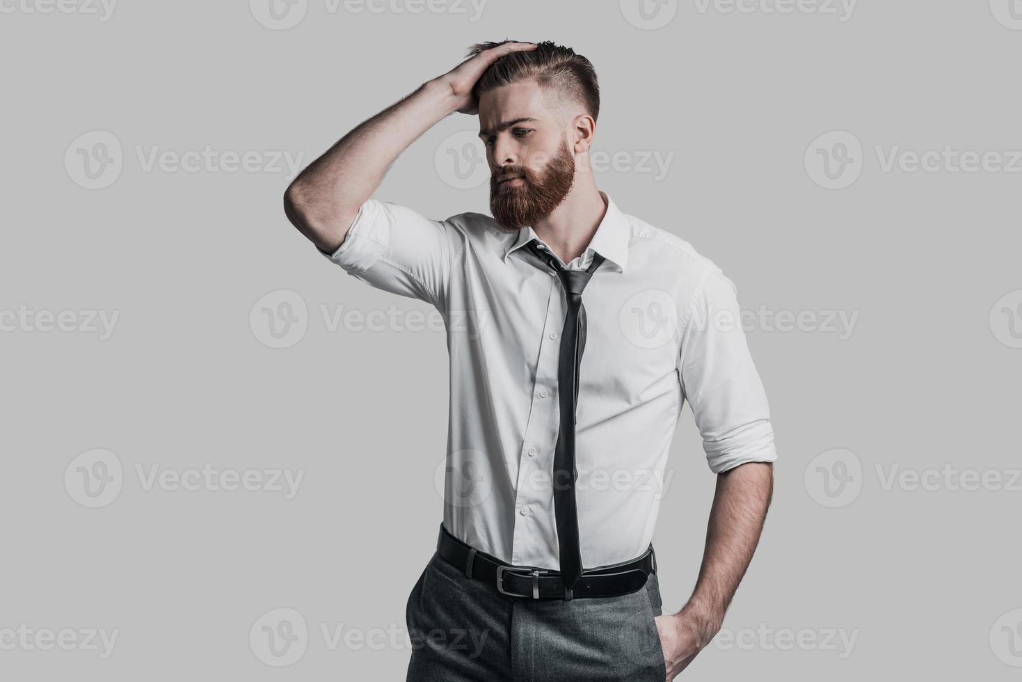 sensazione stanco. giovane bello uomo d'affari Tenere mano su testa e guardare lontano mentre in piedi contro grigio sfondo foto