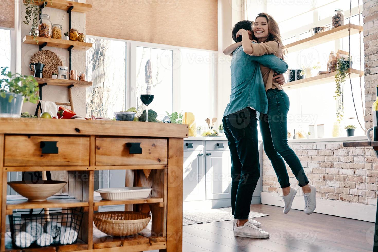 totalmente nel amore. pieno lunghezza di bellissimo giovane coppia nel casuale capi di abbigliamento danza e sorridente mentre in piedi nel il cucina a casa foto