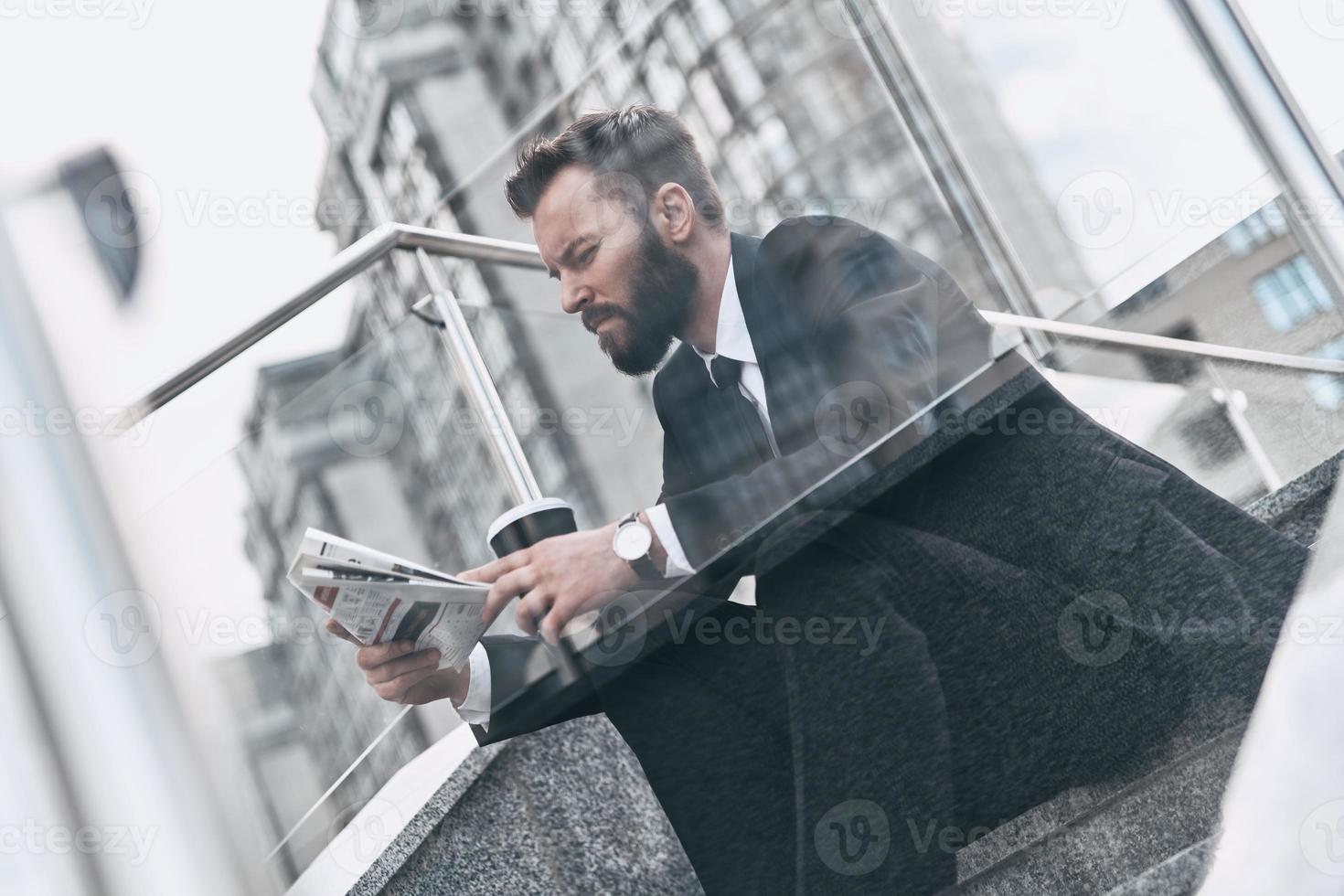 quotidiano notizia digerisce. bene guardare giovane uomo nel pieno completo da uomo lettura un' giornale mentre seduta su il le scale all'aperto foto