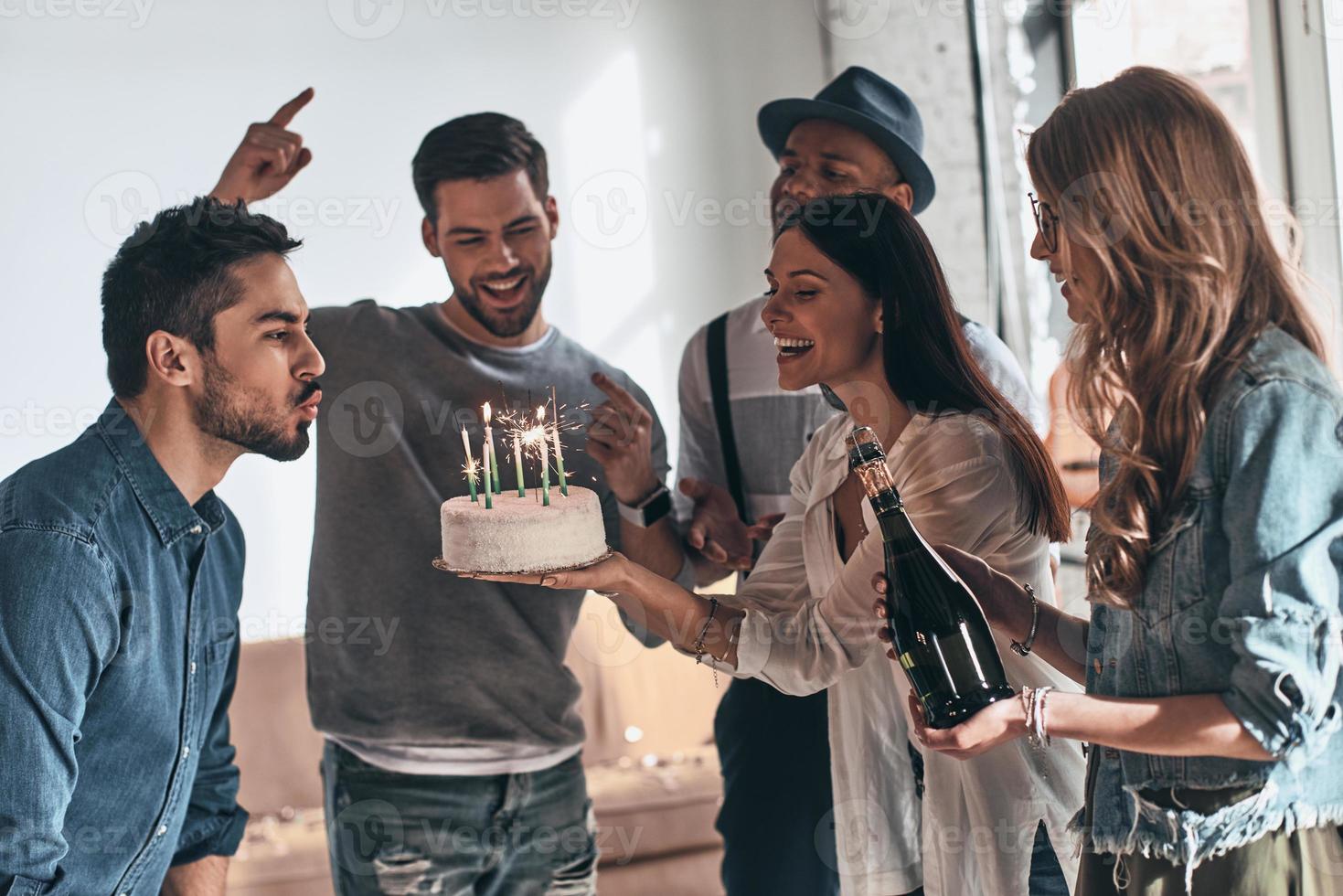 fretta su per rendere un' desiderio. contento giovane uomo soffiaggio candele mentre festeggiare compleanno tra amici foto