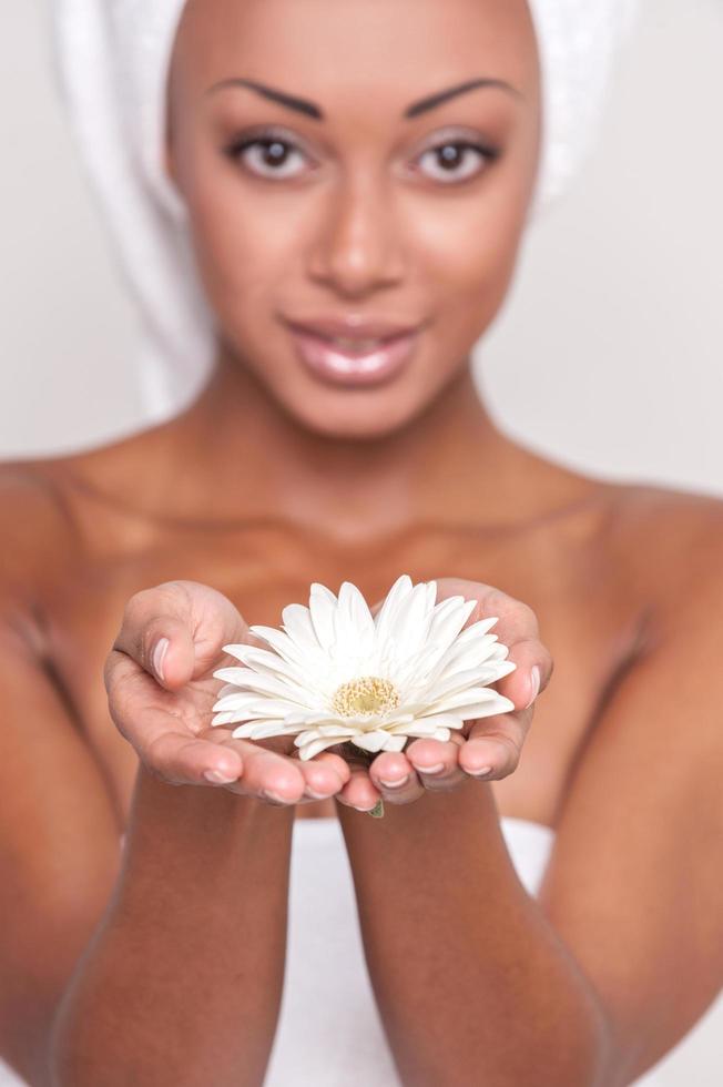 naturale bellezza. bellissimo giovane afro americano A petto nudo donna Tenere fiore nel sua mani e guardare a telecamera mentre isolato su grigio sfondo foto