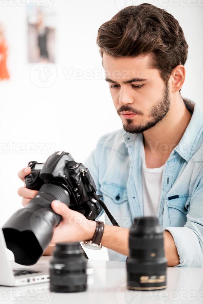 scoperta il giusto sparo. grave giovane uomo Tenere telecamera mentre seduta a il suo Lavorando posto foto