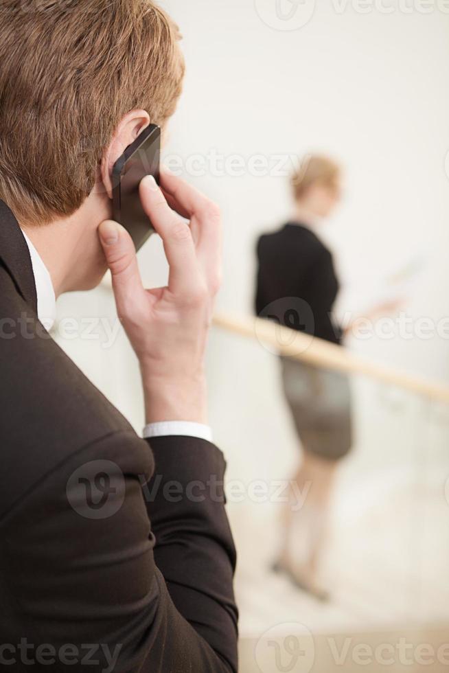 uomo d'affari su il Telefono. posteriore Visualizza di uomo parlando su il mobile Telefono mentre donna in movimento di scala su sfondo foto