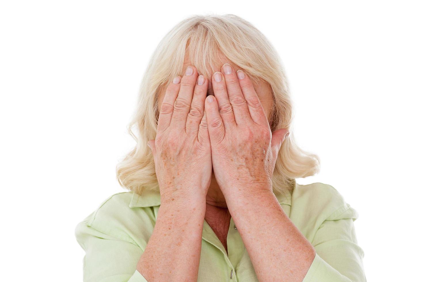 sensazione solitario e senza speranza. depresso anziano donna copertura viso con mani mentre in piedi isolato su bianca sfondo foto