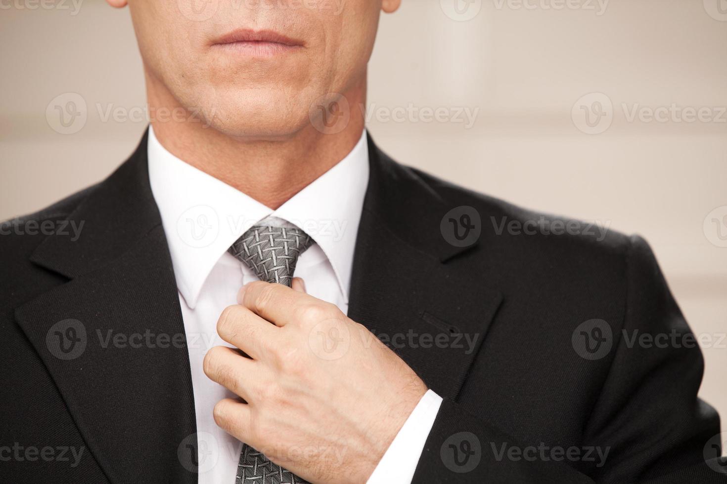 fiducioso e elegante. ritagliata Immagine di fiducioso maturo uomo nel vestito formale regolazione il suo cravatta foto
