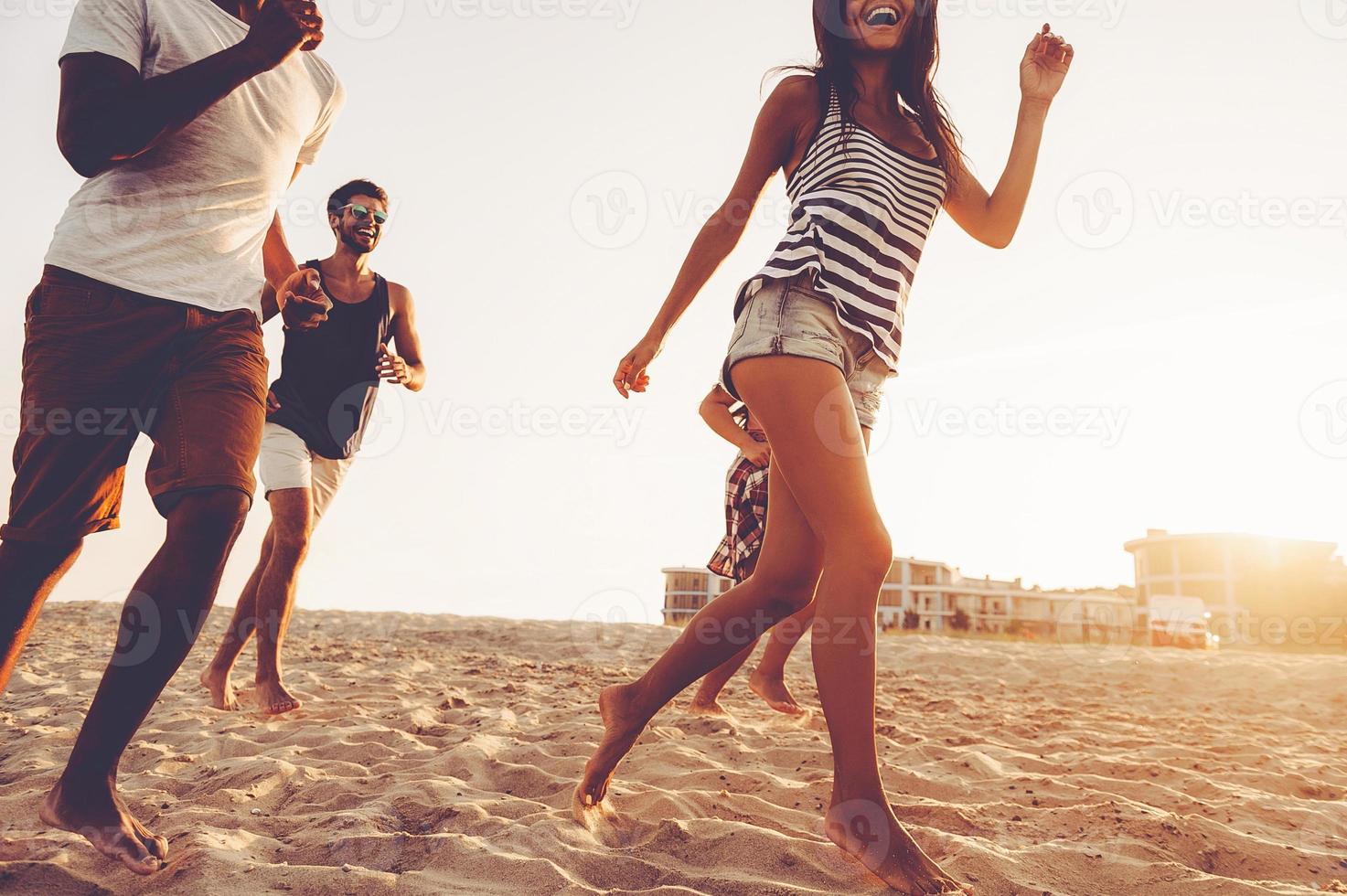 spensierato correre. gruppo di giovane allegro persone in esecuzione lungo il spiaggia e guardare contento foto