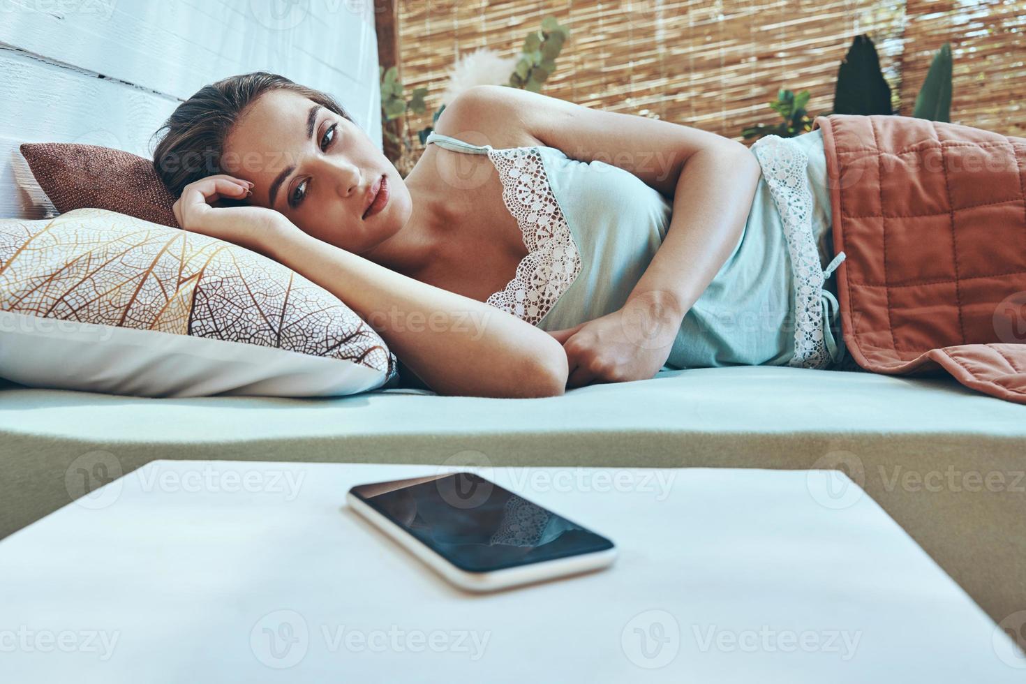bellissimo giovane donna guardare a mobile Telefono mentre dire bugie giù nel domestico letto foto