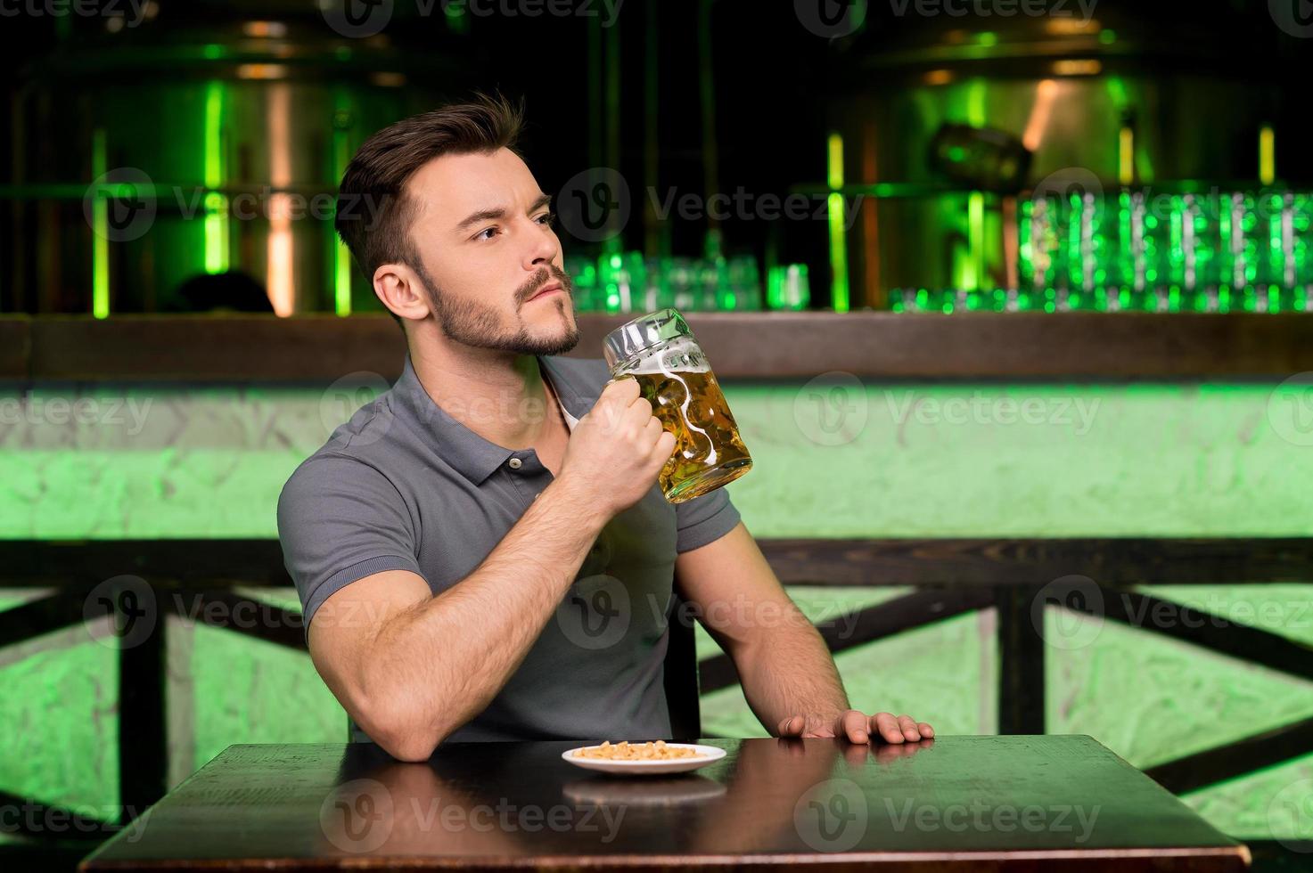 potabile fresco birra. riflessivo giovane uomo Tenere un' boccale con birra e guardare lontano mentre seduta nel bar foto