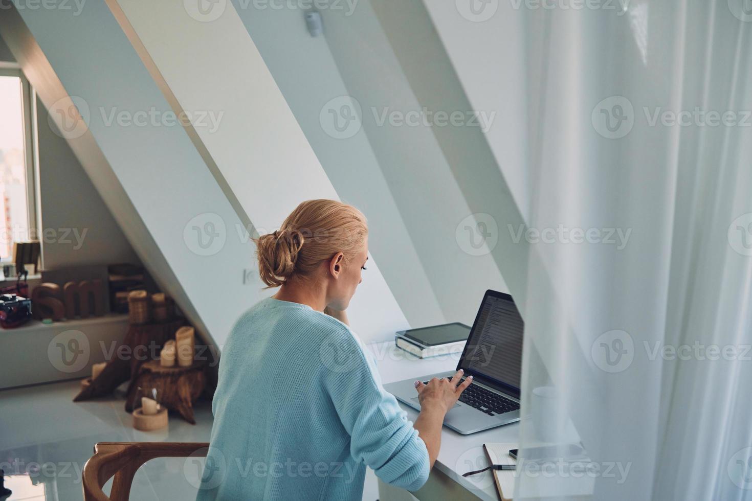 posteriore Visualizza di giovane donna utilizzando il computer portatile mentre Lavorando a casa foto
