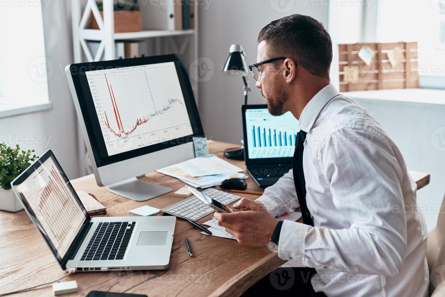 su il modo per successo. giovane uomo d'affari nel vestito formale analizzando dati utilizzando computer mentre seduta nel il ufficio foto