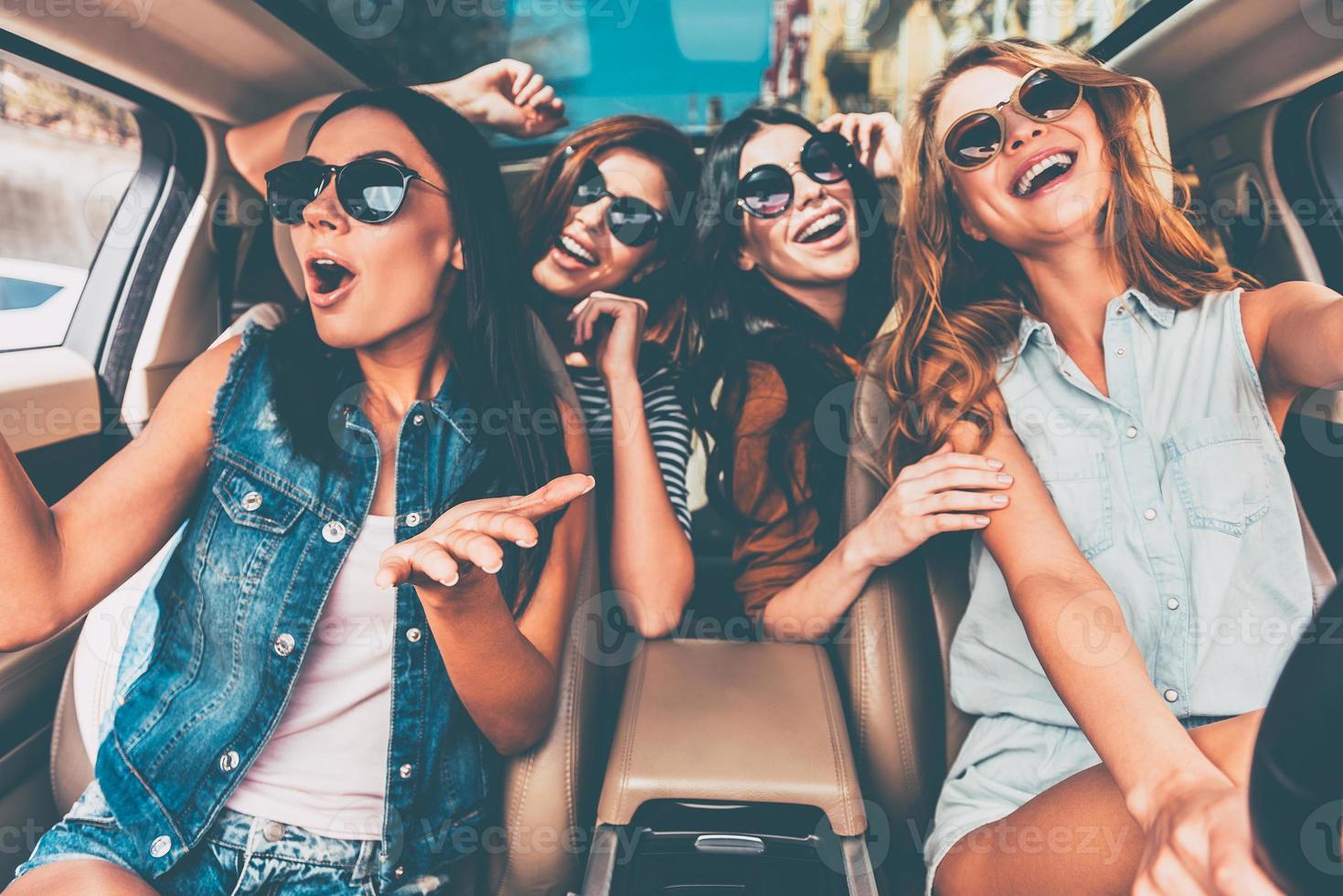 avendo divertimento insieme. quattro bellissimo giovane allegro donne guardare contento e giocoso mentre seduta nel auto foto