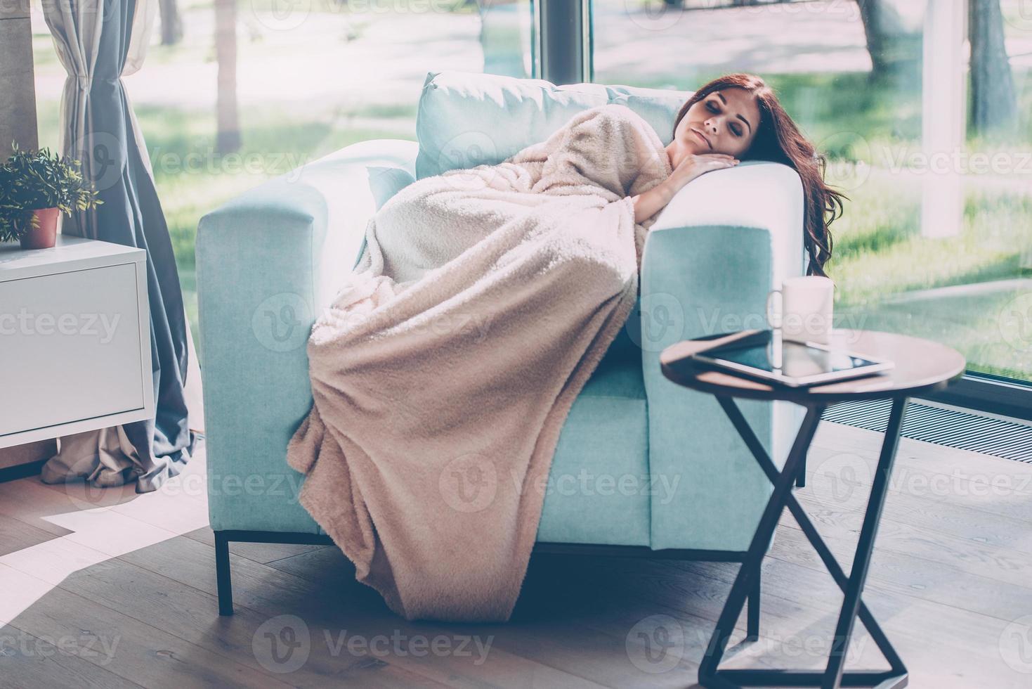 giorno sognare bellezza. bellissimo giovane donna addormentato nel un' grande confortevole sedia a casa mentre essere coperto con coperta foto