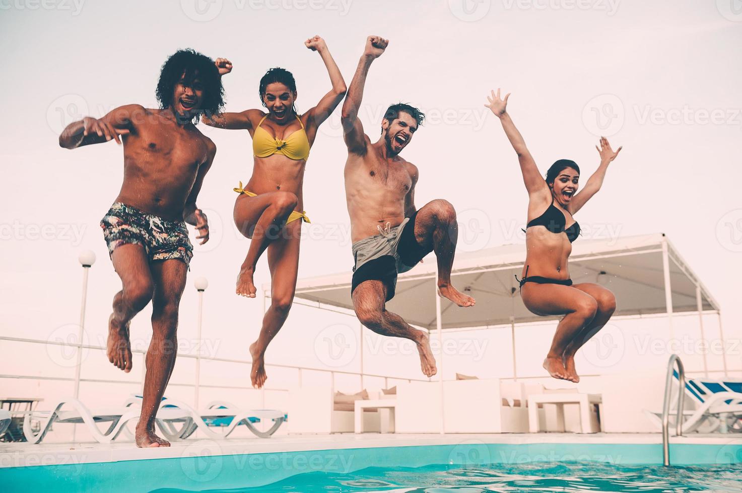 piscina divertimento. gruppo di bellissimo giovane persone guardare contento mentre salto in il nuoto piscina insieme foto