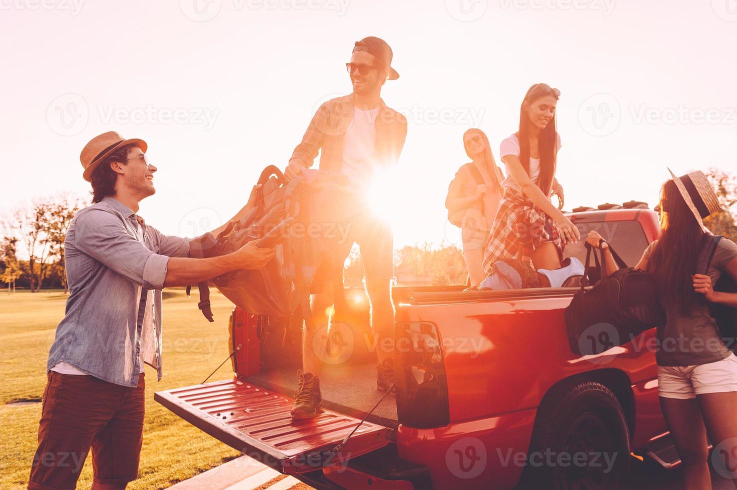 preparazione per strada viaggio. bellissimo giovane persone Caricamento in corso loro zaini per Raccogliere camion e guardare contento con tramonto nel il sfondi foto