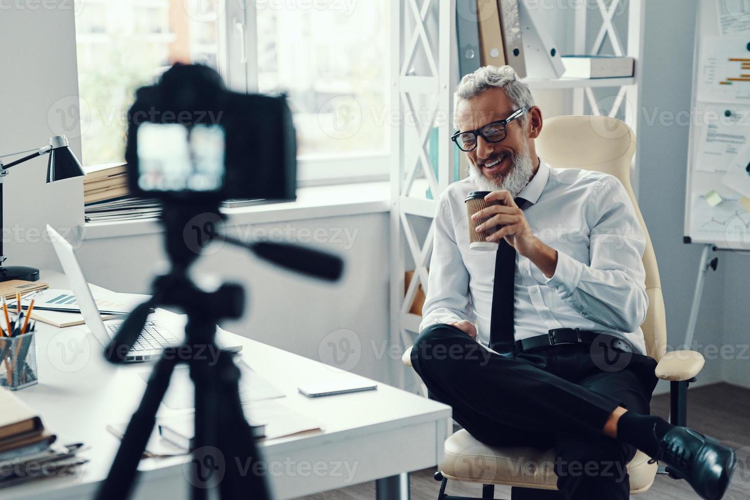 contento maturo uomo nel elegante camicia e cravatta telling qualcosa e sorridente mentre fabbricazione sociale media video foto