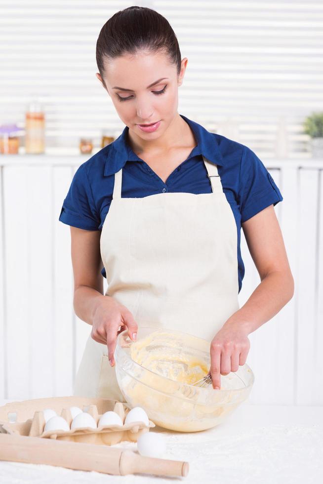 lei è un' Pasticcino esperto. bellissimo giovane donna miscelazione Impasto con filo frusta mentre in piedi nel un' cucina foto