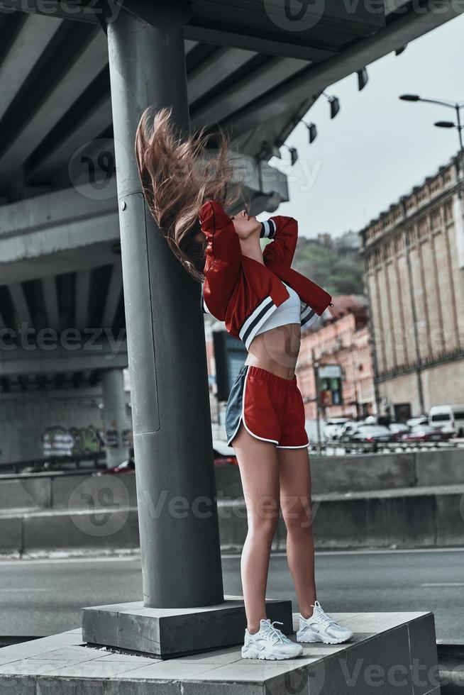 bellezza nel movimento. pieno lunghezza di attraente giovane donna nel sport capi di abbigliamento in posa mentre in piedi all'aperto foto