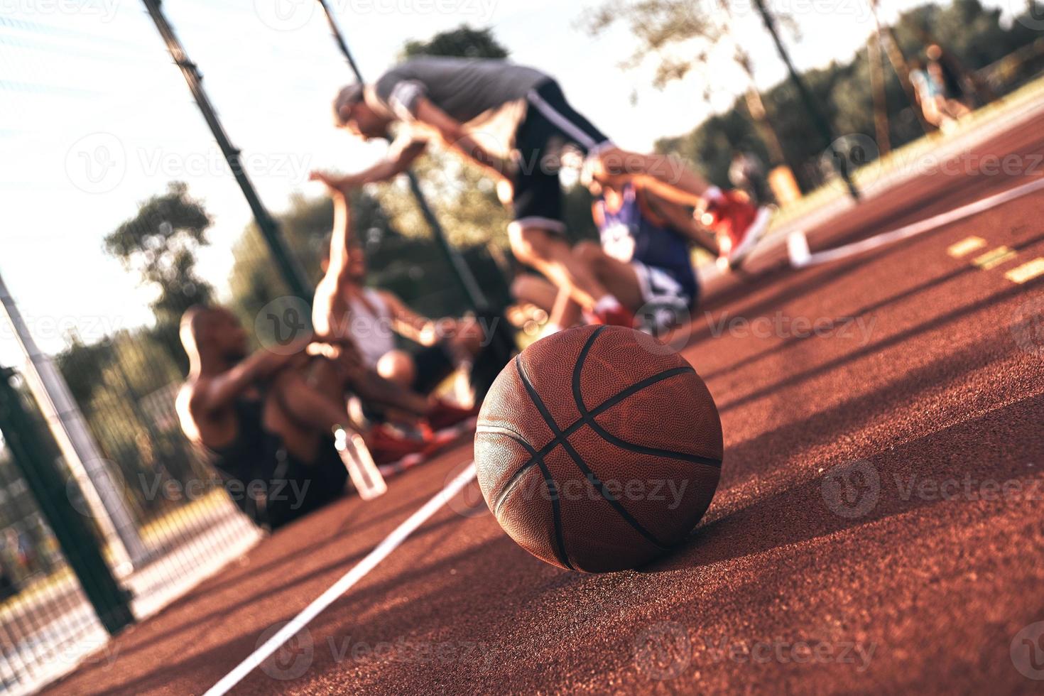 gioco è Sopra. gruppo di giovane uomini nel gli sport capi di abbigliamento comunicare mentre seduta su il pallacanestro campo all'aperto foto