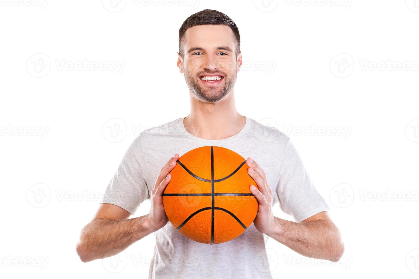 io amore pallacanestro. fiducioso giovane uomo Tenere pallacanestro palla e sorridente mentre in piedi contro bianca sfondo foto