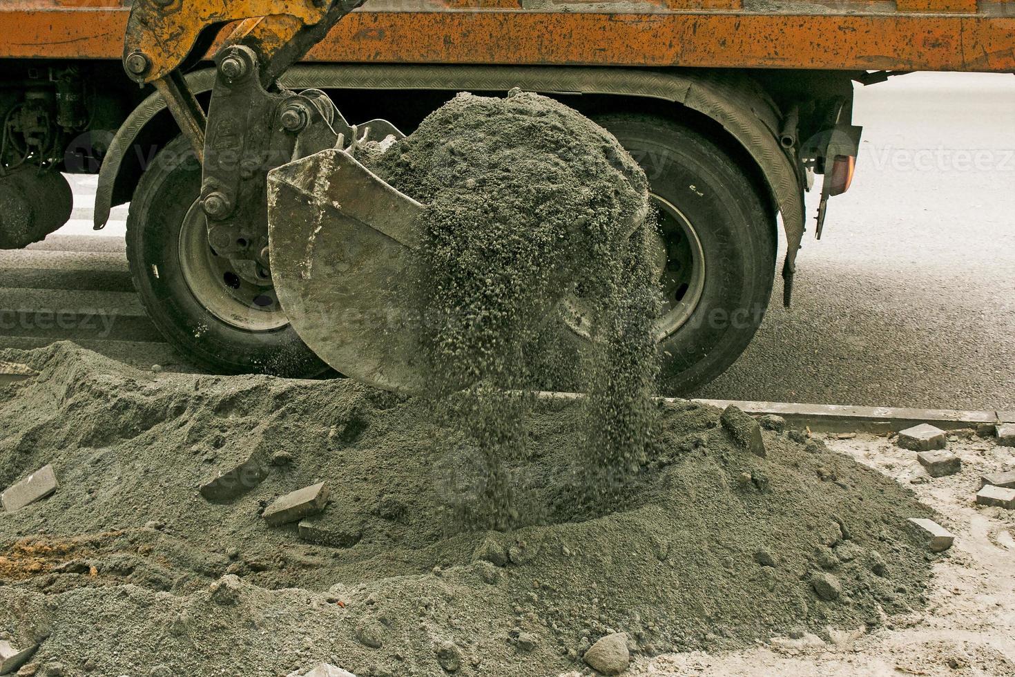 strada lavori su il città strada. il scavatrice secchio raccoglie il vecchio marciapiede e carichi esso in un' cumulo di rifiuti camion foto