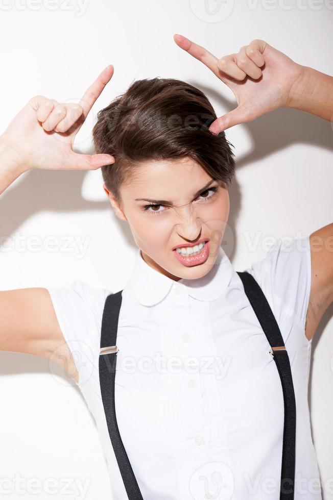 io am un' cattivo ragazza giovane corto capelli donna nel bianca camicia e giarrettiere fabbricazione corna con dita e smorfie foto