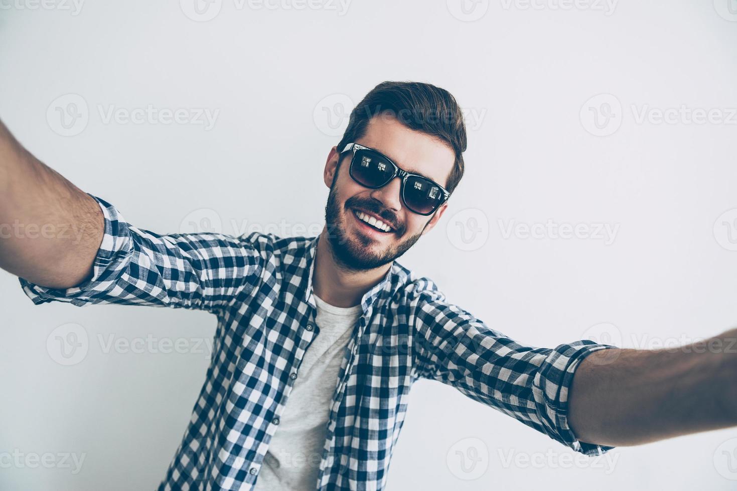 autoscatto tempo studio tiro di bello giovane uomo nel occhiali da sole fabbricazione autoscatto e sorridente foto