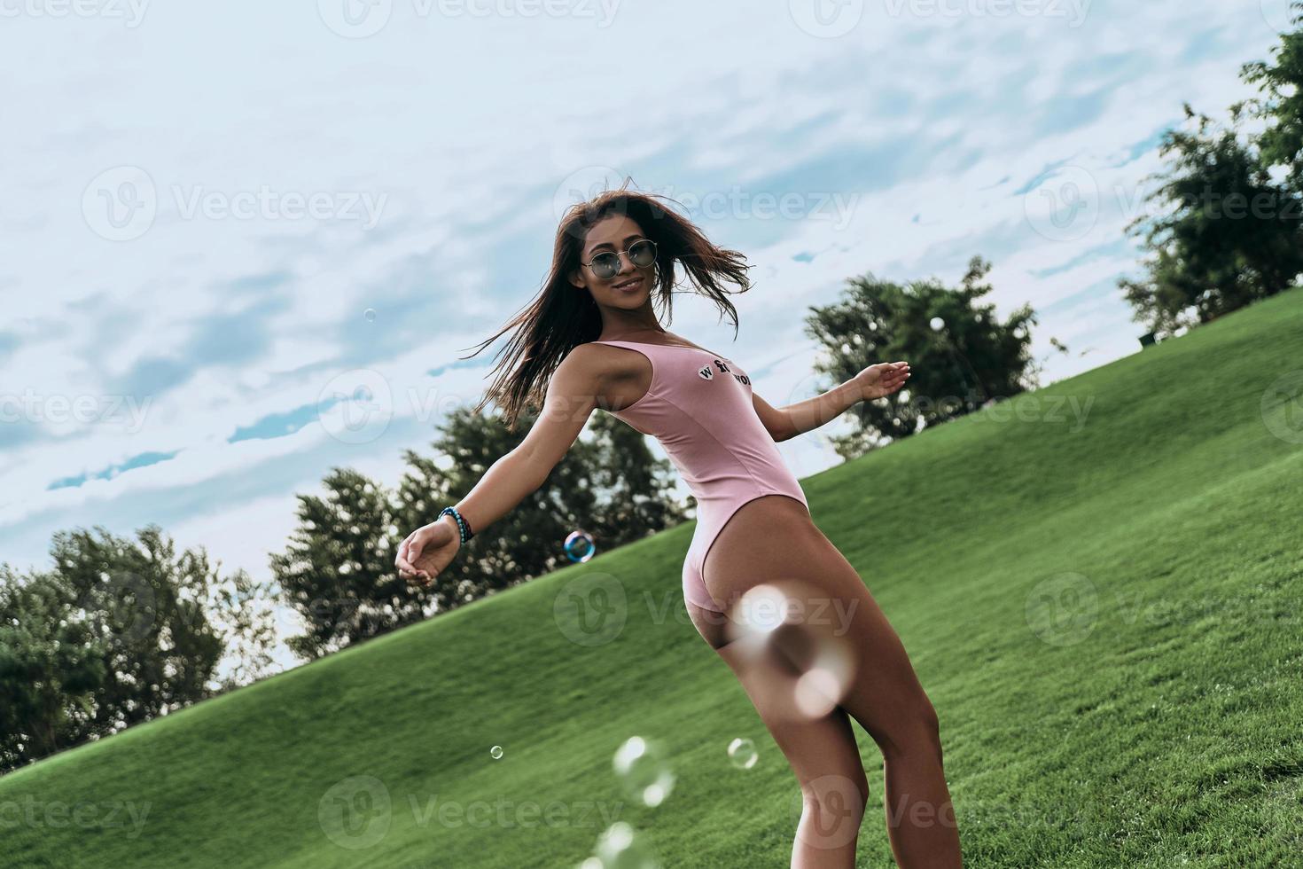 attraente giovane donna nel costumi da bagno conservazione braccia disteso e sorridente mentre a piedi all'aperto foto