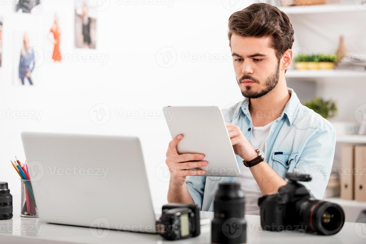 scoperta un' giusto foto per il suo progetto. fiducioso giovane uomo Lavorando su digitale tavoletta mentre seduta a il suo Lavorando posto