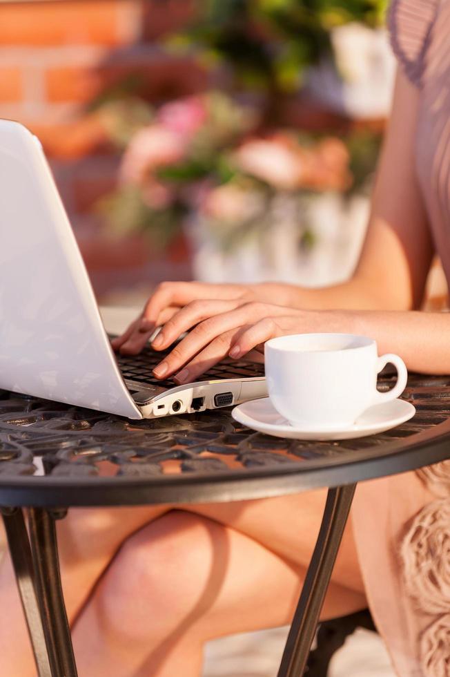 utilizzando vantaggi di gratuito Wifi. ritagliata Immagine di donna Lavorando a il computer portatile mentre seduta a il all'aperto bar foto