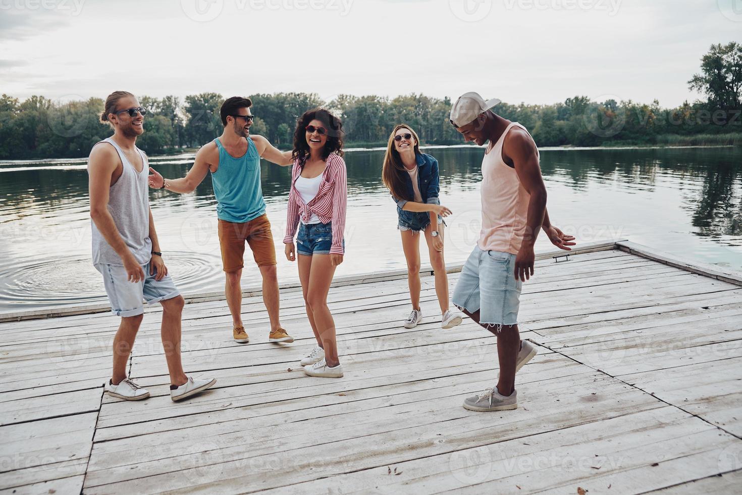 fuga a partire dal il città. pieno lunghezza di contento giovane persone nel casuale indossare sorridente e Esprimere a gesti mentre godendo spiaggia festa foto