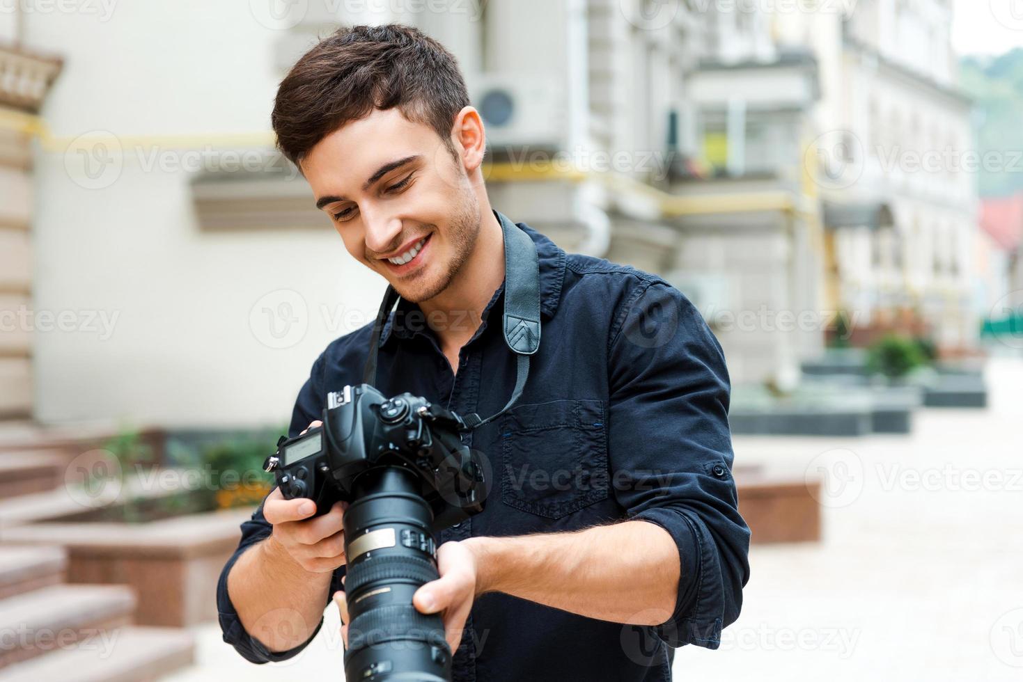 scoperta il giusto sparare. contento giovane uomo Tenere telecamera e sorridente mentre in piedi all'aperto foto