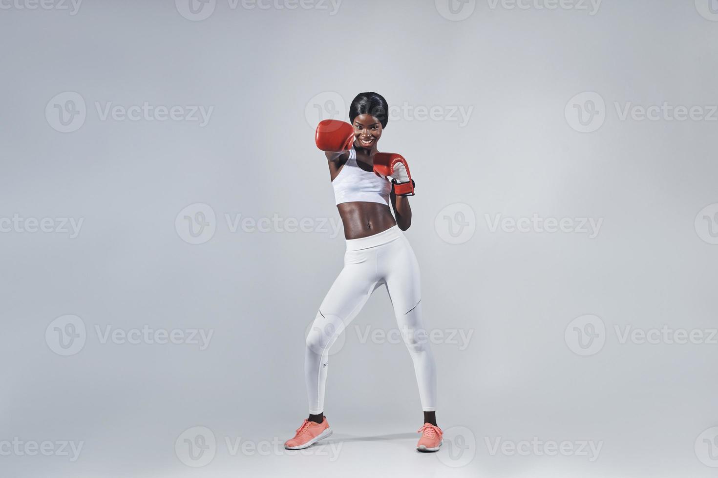 bellissimo giovane africano donna nel boxe guanti esercizio mentre in piedi contro grigio sfondo foto