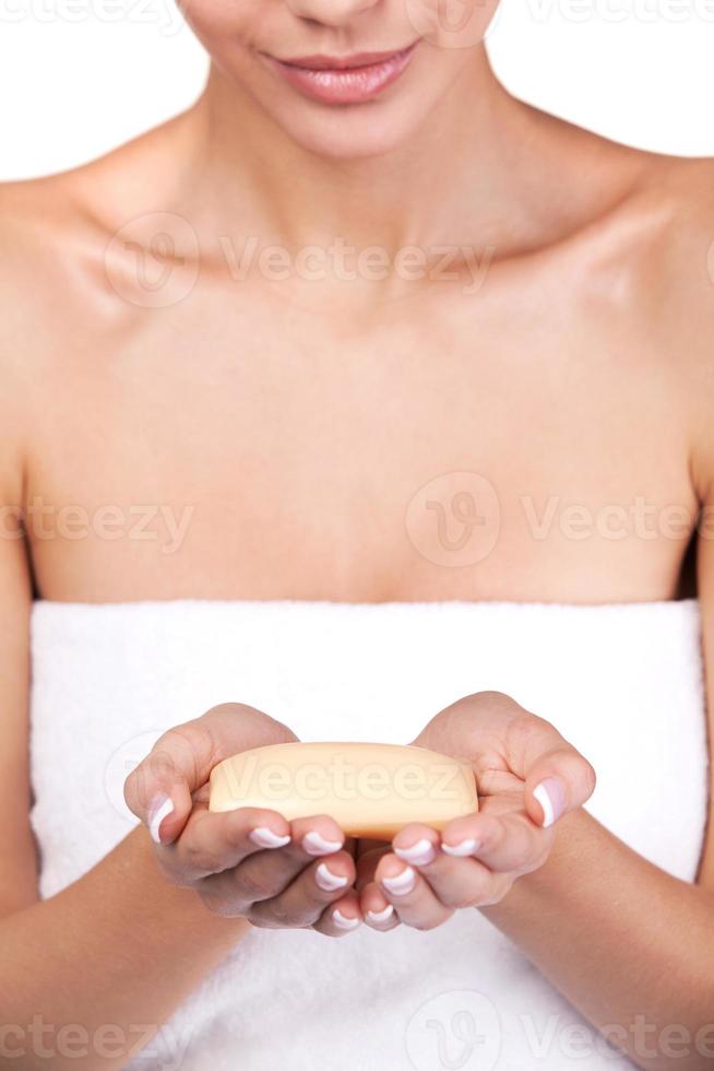 freschezza nel sua mani. ritagliata Immagine di bellissimo giovane donna avvolto nel asciugamano Tenere un' sapone bar mentre in piedi contro grigio sfondo foto