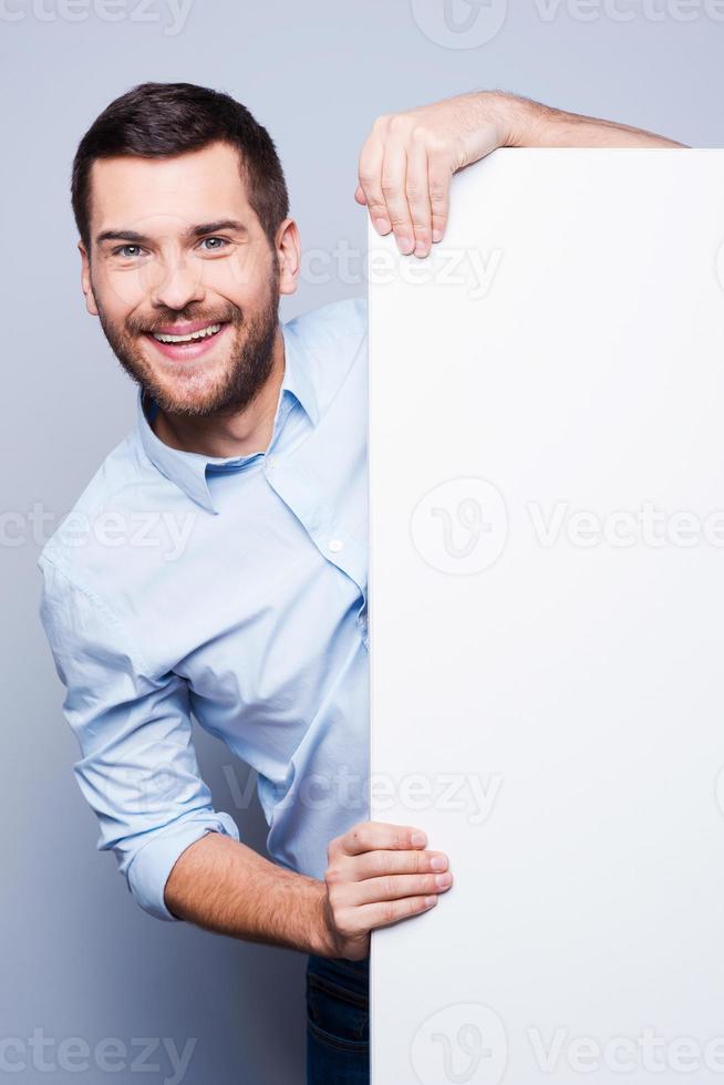 pubblicità il tuo Prodotto. bello giovane uomo pendente a copia spazio e sorridente mentre in piedi contro grigio sfondo foto