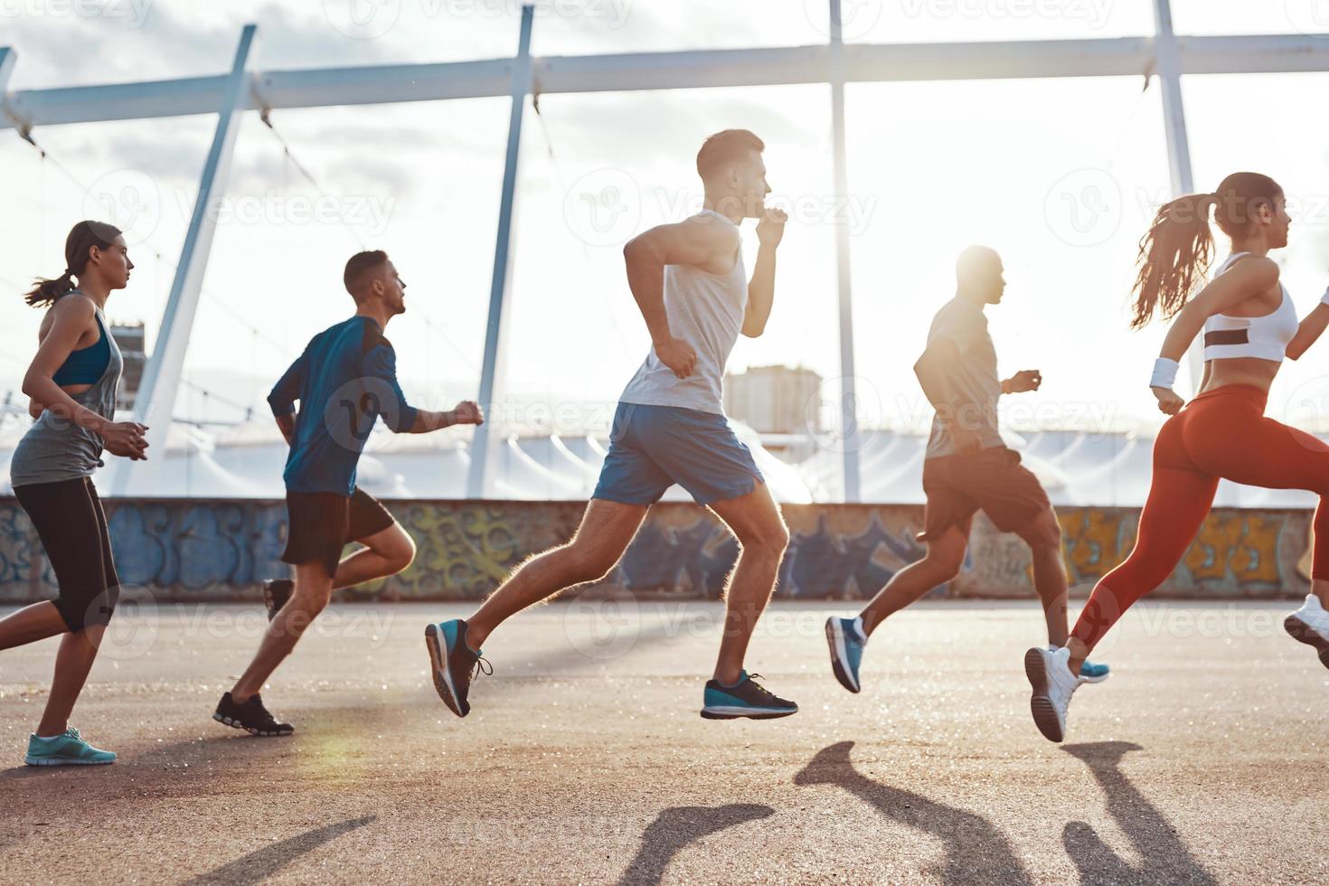 pieno lunghezza di persone nel gli sport capi di abbigliamento jogging mentre esercizio su il marciapiede all'aperto foto