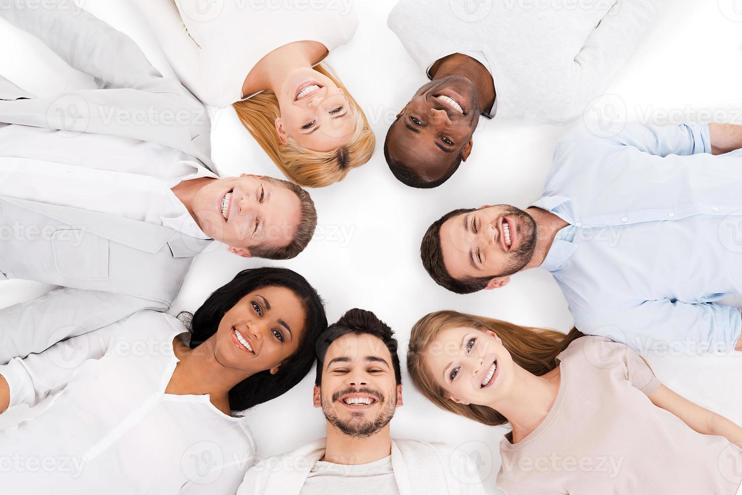 insieme noi siamo più forte. superiore Visualizza di allegro gruppo di multietnico persone posa su loro schiene e sorridente mentre in piedi isolato su bianca foto