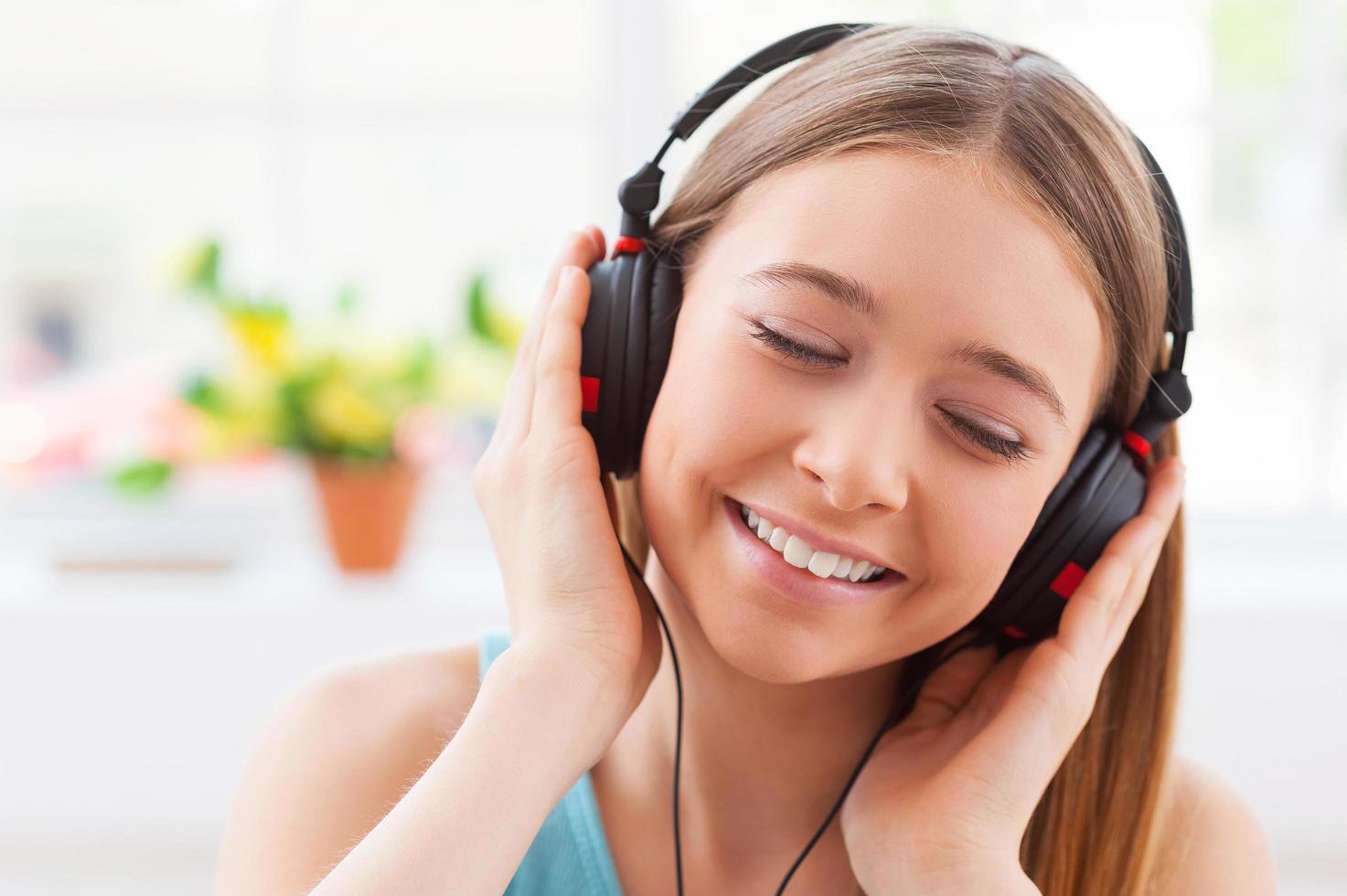 giorno sognare con sua preferito musica. allegro adolescenziale ragazza nel cuffie ascoltando per il musica e conservazione occhi chiuso mentre seduta nel sua appartamento foto