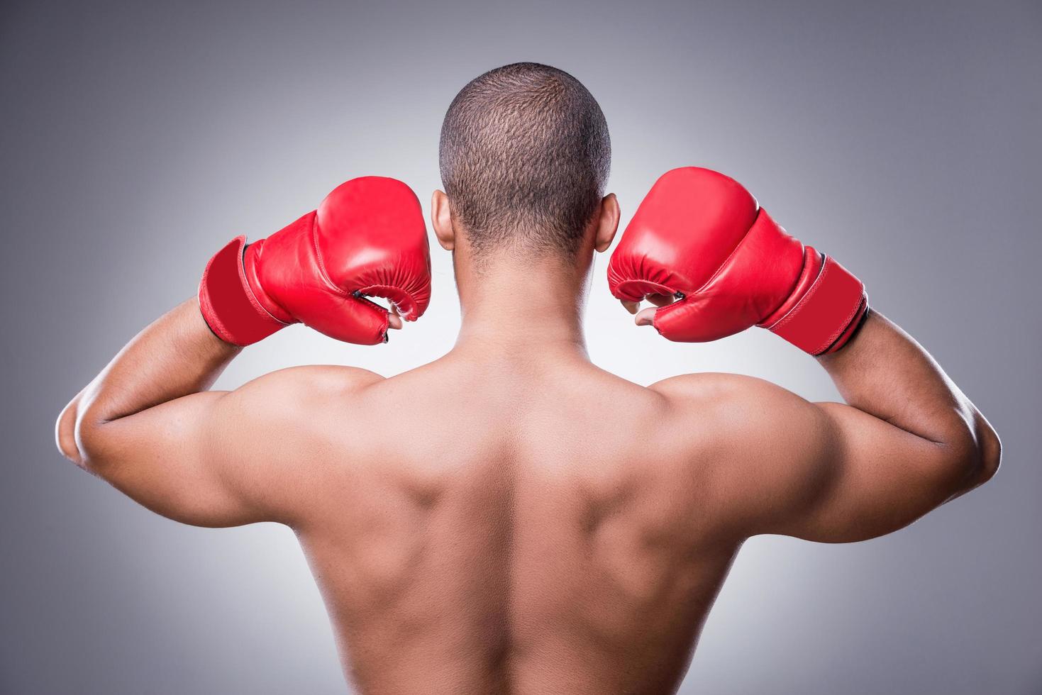 semplicemente il migliore. posteriore Visualizza di A petto nudo africano uomo nel boxe guanti in piedi contro grigio sfondo foto