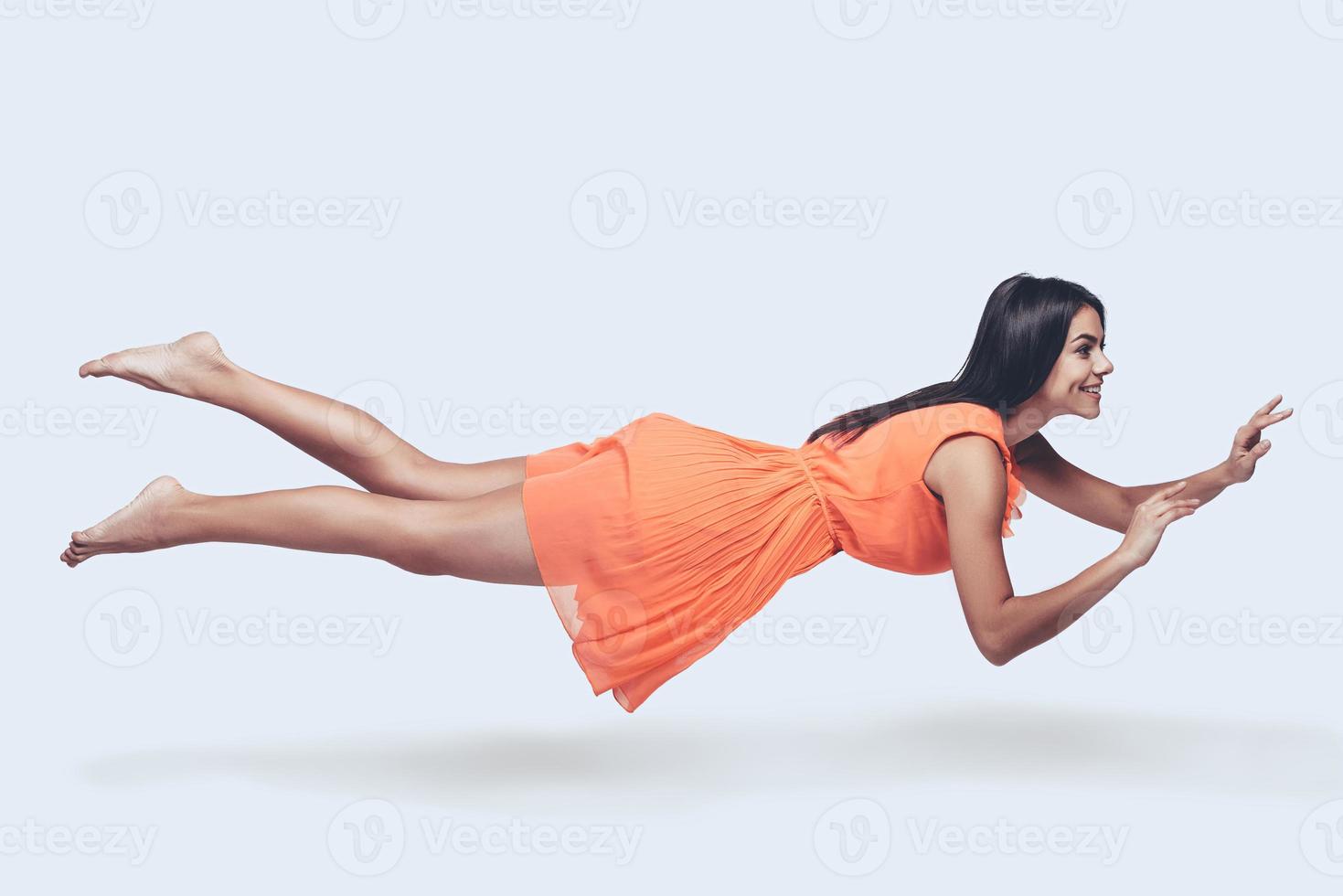 bellezza nel il aria. pieno lunghezza studio tiro di attraente giovane donna nel arancia vestito librarsi nel aria e sorridente foto
