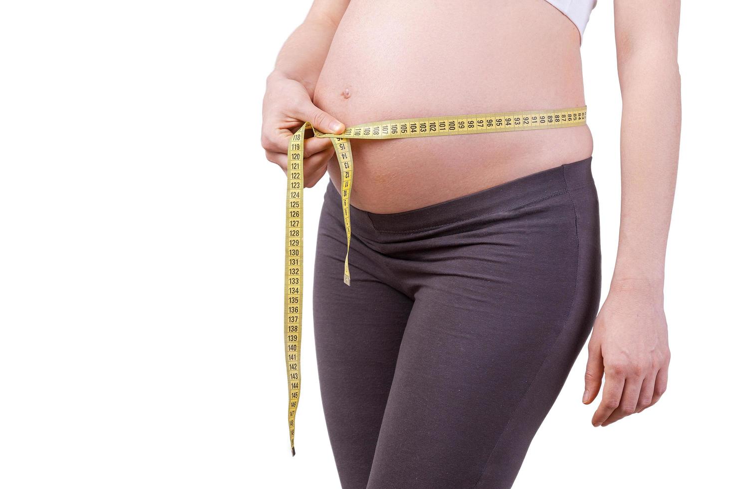 misurazione sua incinta gonfiarsi. ritagliata Immagine di incinta donna misurazione sua incinta pancia mentre in piedi isolato su bianca foto