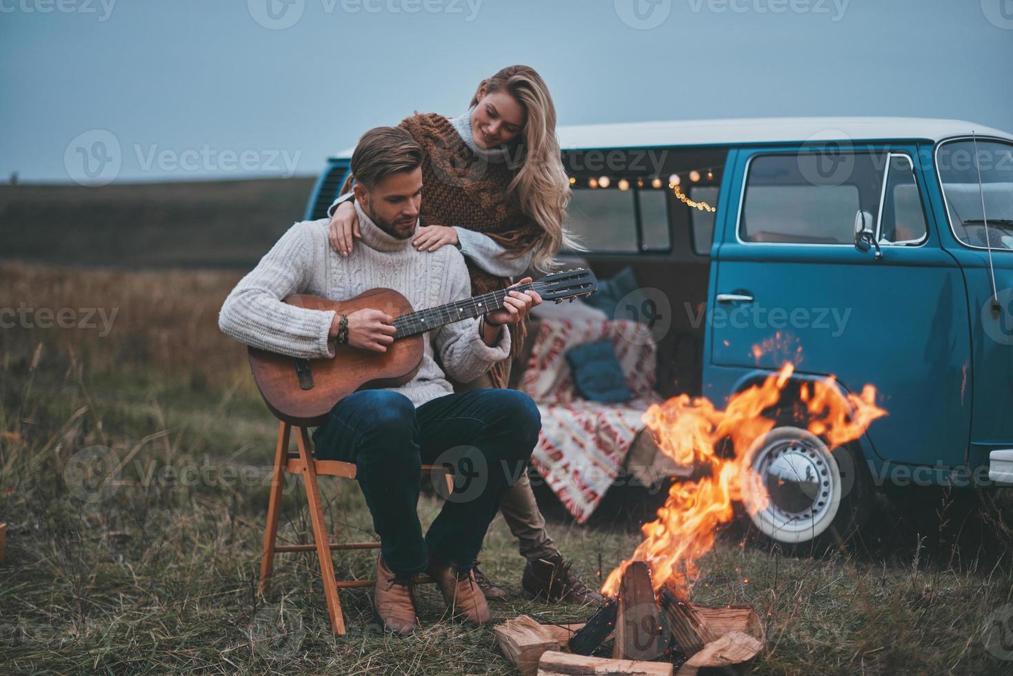 amore e fiducia. bello giovane uomo giocando chitarra per il suo attraente fidanzata mentre seduta di il falò foto