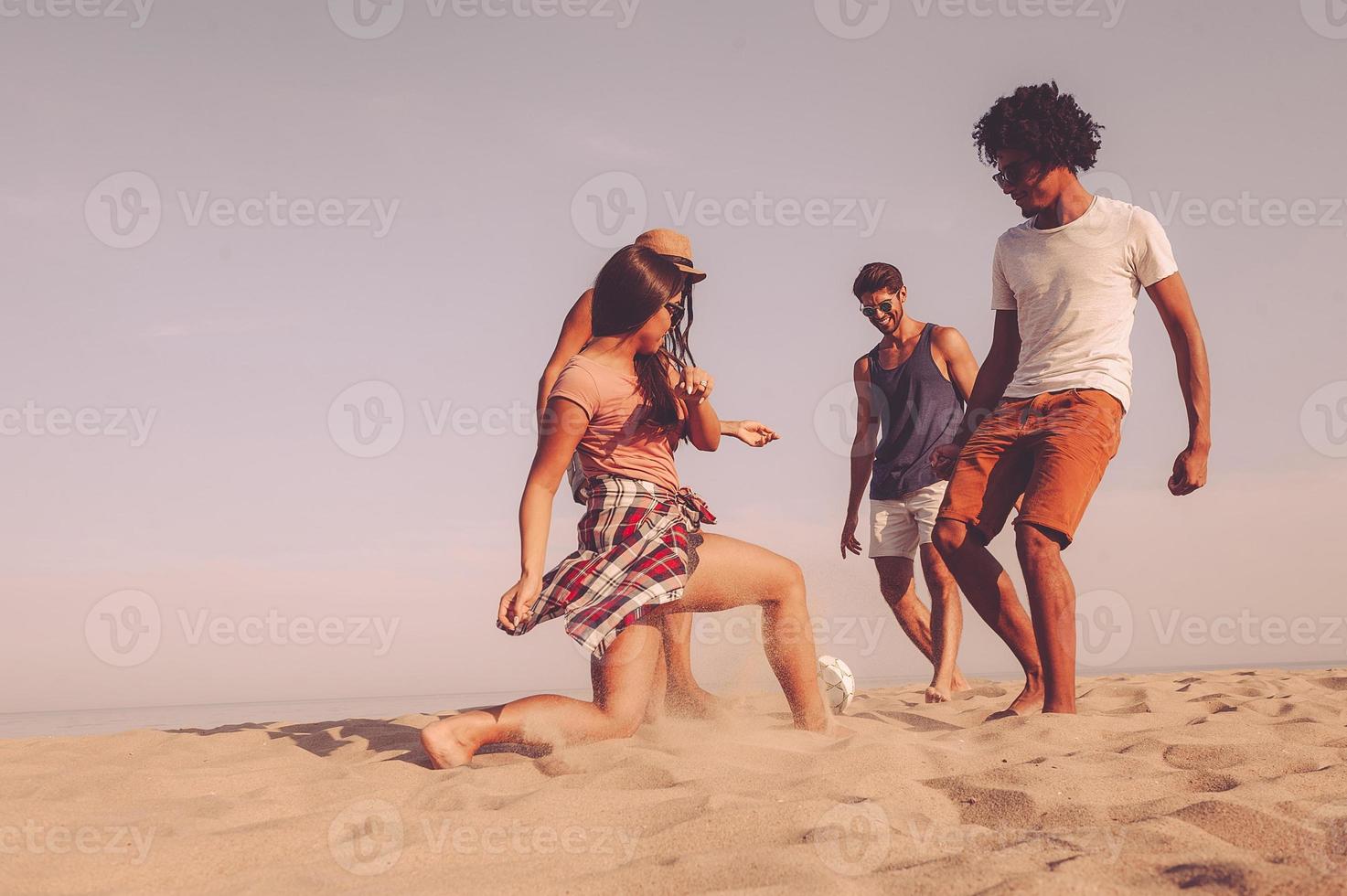 godendo spiaggia tempo insieme. gruppo di allegro giovane persone giocando con calcio palla su il spiaggia foto