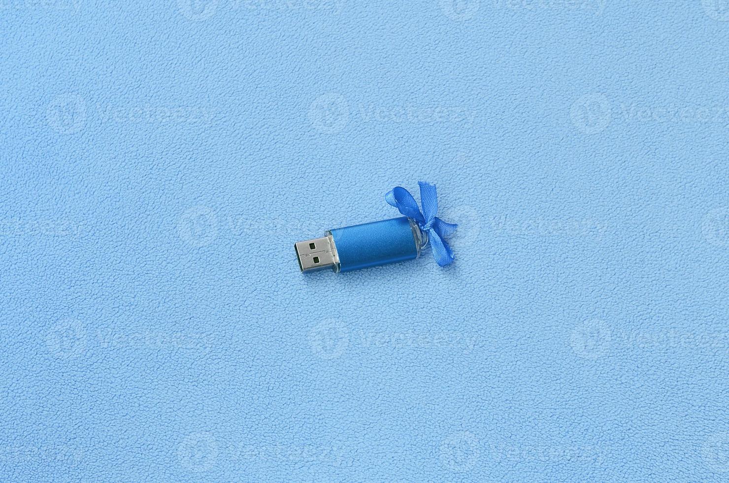 brillante blu USB veloce memoria carta con un' blu arco bugie su un' coperta di morbido e peloso leggero blu vello tessuto. classico femmina regalo design per un' memoria carta foto