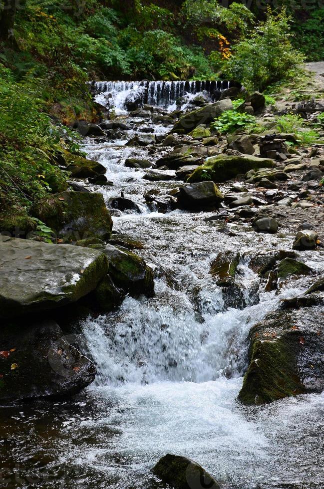 avvicinamento Immagine di un' piccolo selvaggio cascata nel il modulo di corto flussi di acqua fra montagna pietre foto