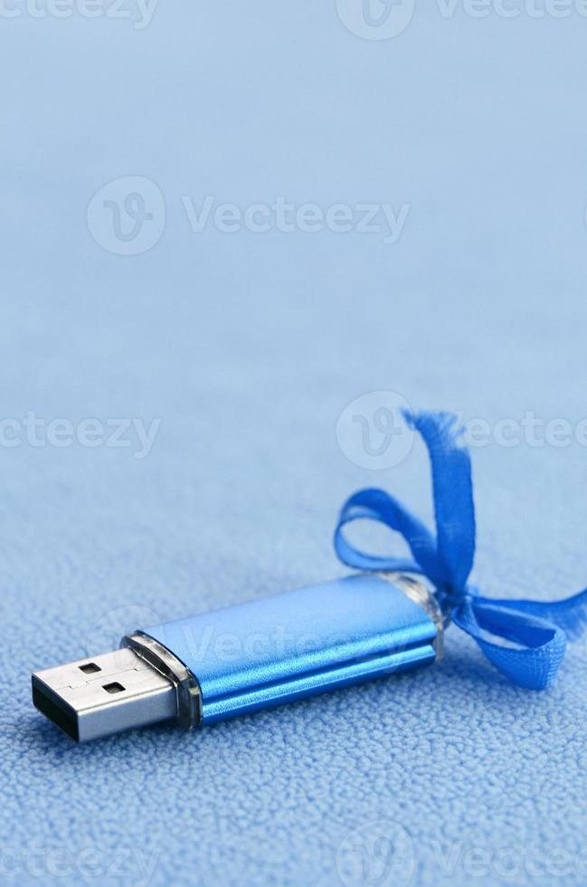 brillante blu USB veloce memoria carta con un' blu arco bugie su un' coperta di morbido e peloso leggero blu vello tessuto. classico femmina regalo design per un' memoria carta foto