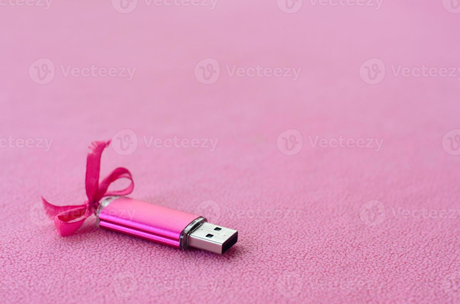 brillante rosa USB veloce memoria carta con un' rosa arco bugie su un' coperta di morbido e peloso leggero rosa vello tessuto. classico femmina regalo design per un' memoria carta foto